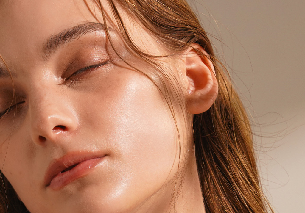 Close-up of a woman’s serene face with eyes closed, glowing smooth skin, and soft natural makeup.