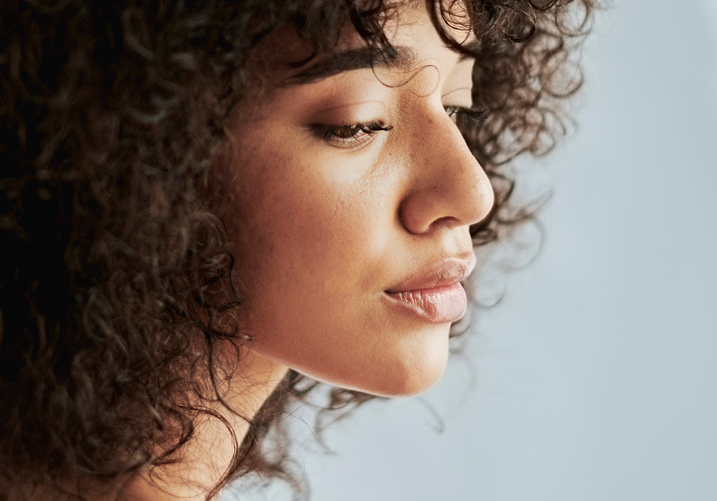 Side profile of a woman with curly hair and natural glowing skin, looking downward with a serene expression.