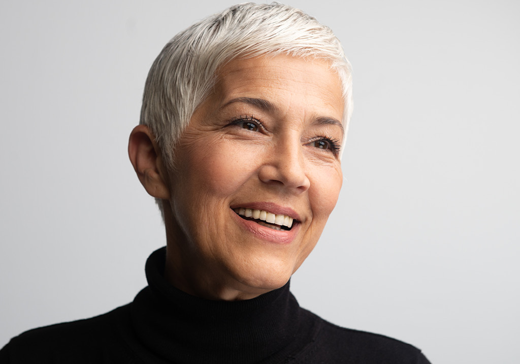 Smiling older woman with short silver hair wearing a black turtleneck, looking slightly off camera.