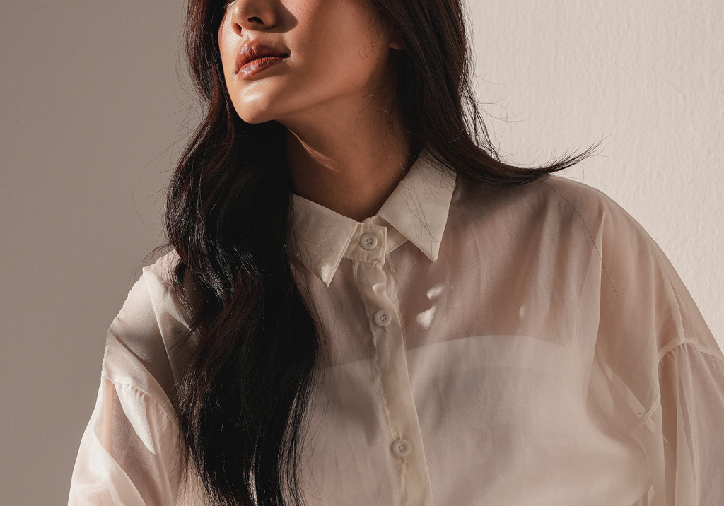 Partial view of a woman in a sheer white blouse, softly lit, with her face turned slightly upward.
