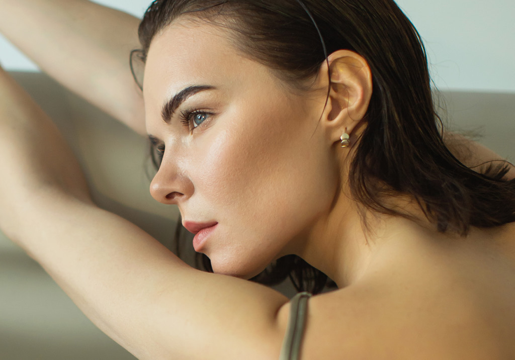 Profile view of a woman with smooth skin and wet hair, arms raised, gazing into the distance.