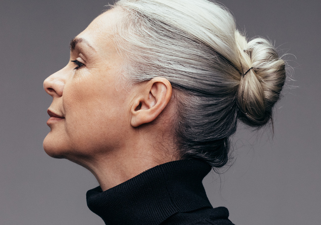 Elegant older woman with silver hair in a neat bun, wearing a black turtleneck, in profile view.