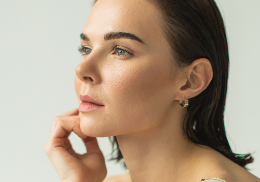 Close-up side profile of a woman with smooth glowing skin and wet dark hair, resting her hand near her chin.